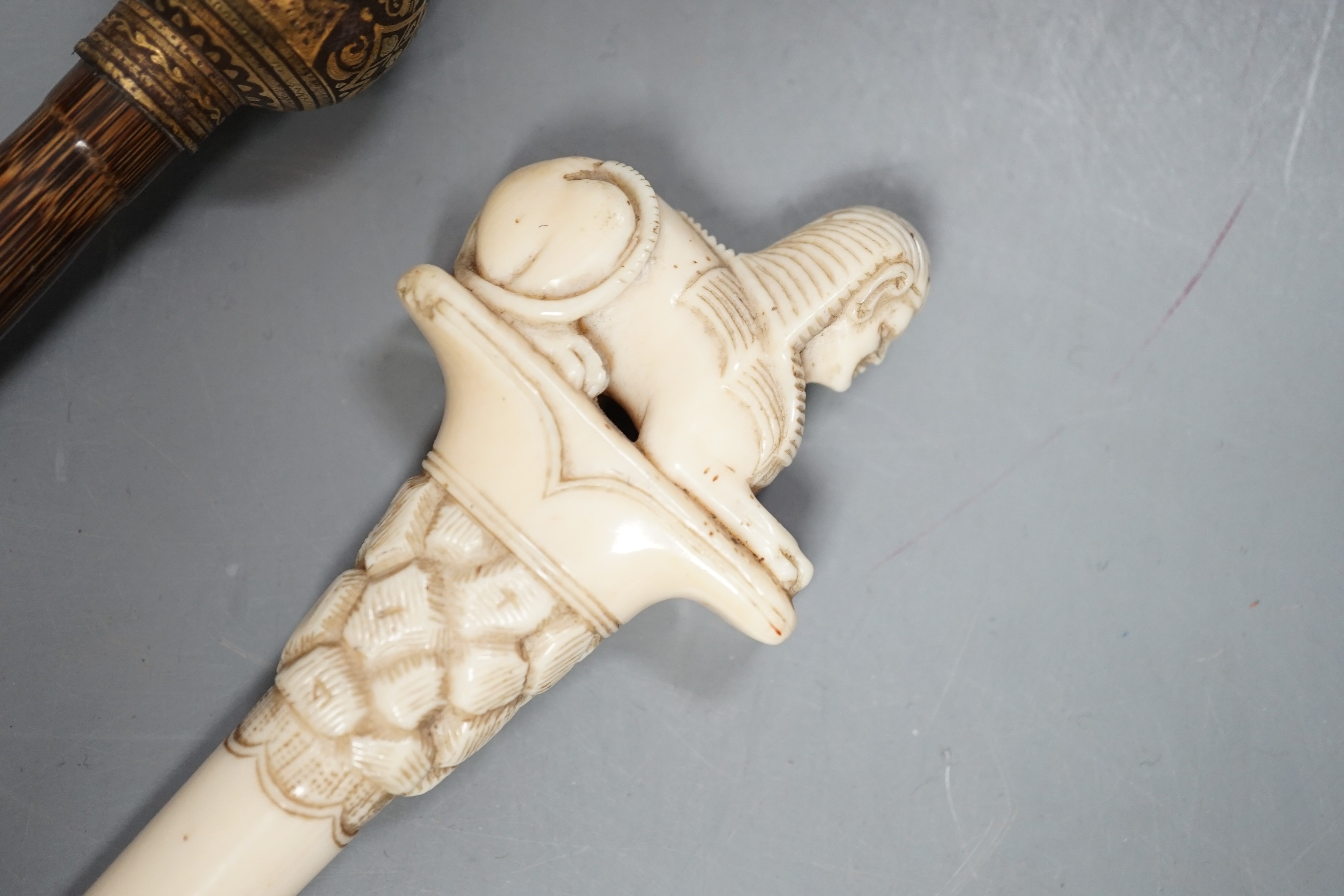 An early 20th century ivory ‘sphinx’ parasol handle, 84cm, together with another gold and iron damascened parasol handle, 62cm